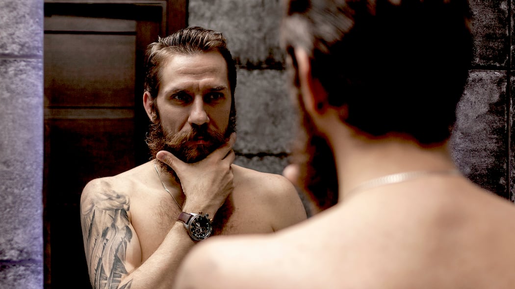 Hau(p)tsache männlich! Hautpflege für Männer: Ein Mann mit Bart betrachtet sich im Spiegel.