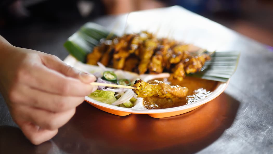 So schlagen die Ferien nicht auf den Magen Ein Mann isst Satay-Spiesse.