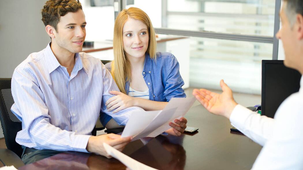 Müssen wir damit zum Notar? Ein Paar befindet sich auf einem Notariat und erhält zwei Dokumente zur Unterschrift ausgehändigt.