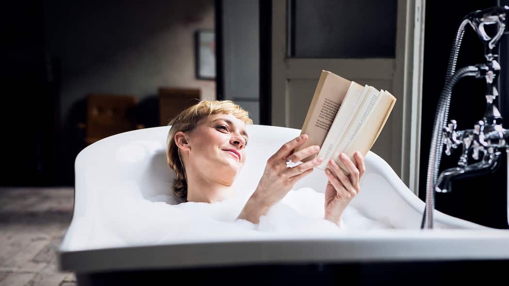 Die Kunst des Müssiggangs Eine Frau liegt in der Badewanne und liest ein Buch