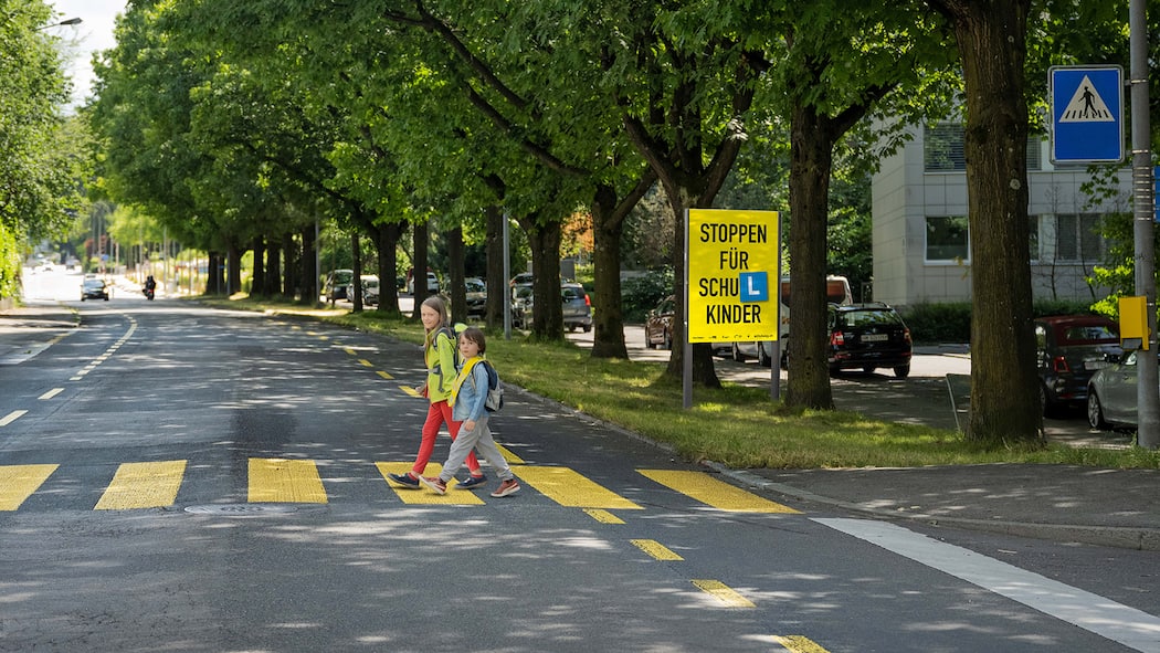 Autofahrer müssen Rücksichtnahme lernen Kinder, die einen Fussgängerstreifen überqueren. Im Hintergrund die Plakatkampagne, die zu mehr Rücksicht aufruft.