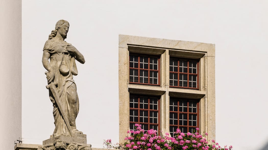 Probleme mit Strafbefehlen – doch die Politik handelt nicht Rathausbrunnen mit Justitia in Brugg, Aargau. Im Hintergrund ein Haus mit einem Fenster mit Geranien