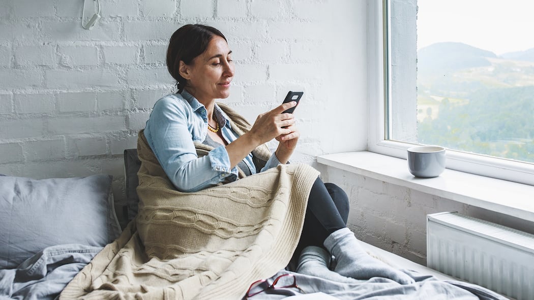 7 Apps für mehr Entspannung Entspannte Frau sitzt mit Handy auf Sofa