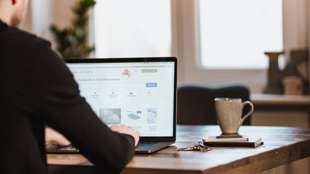 Betrüger kapern Benutzerkonten Mann schaut am Tisch auf Laptop die Website von anibis.ch an