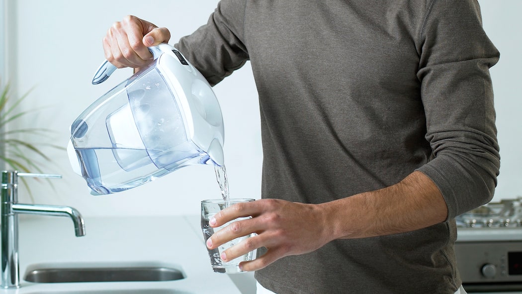 Warum Wasser filtern meist überflüssig ist Mann schenkt gefiltertes Leitungswasser in ein Glas ein