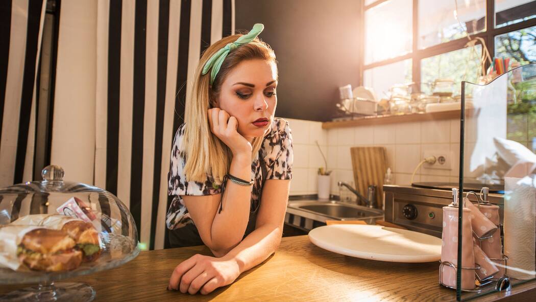 Muss ich die Fehlstunden nacharbeiten? Frau blickt betrübt und stützt sich mit der rechten Hand auf einem Küchenthresen ab