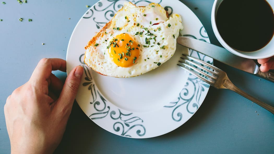 Warum Eiweisse so wichtig sind für eine gesunde Ernährung Eine Frau sitzt am Tisch, vor ihr liegt ein Spiegelei auf dem Teller.