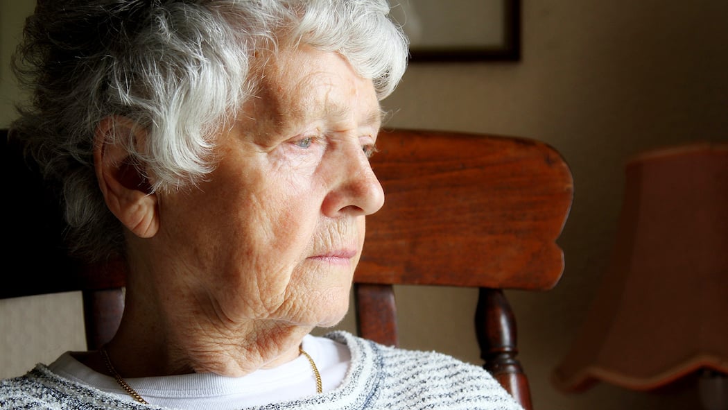Welche Anzeichen alarmieren sollten Eine Seniorin sitzt am Fenster und schaut mit schwermütigem Blick nach draussen.