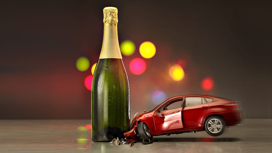 Wie viel Promille liegen drin? Symbolisches Bild in welchem ein Spielzeugauto in eine Sektflasche kracht