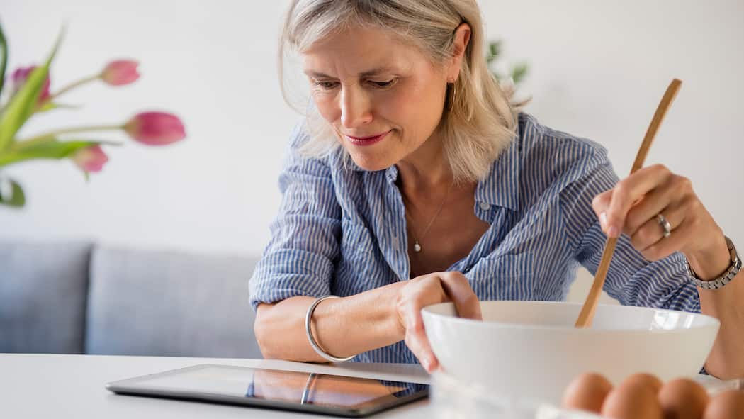 8 praktische Apps für den Alltag Eine Frau schaut auf ihr Tablet während dem Kochen.