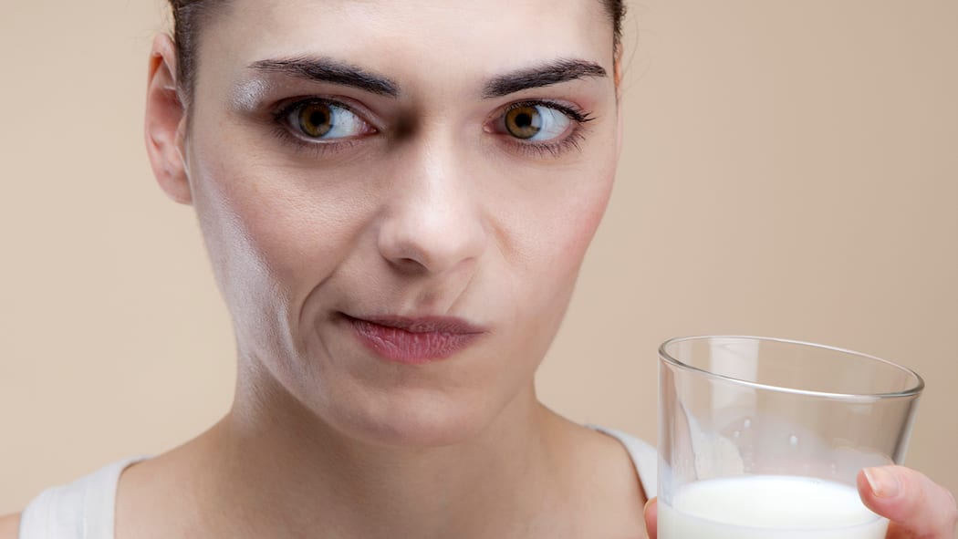 Wenn Milch Bauchweh macht Eine Frau mit einem Glas Milch in der Hand schaut skeptisch.