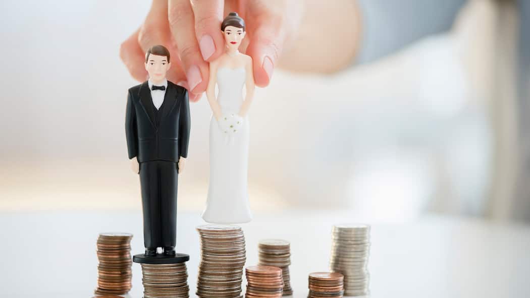 Wann ist Gütertrennung sinnvoll? Zwei Figuren einer Braut und eines Bräutigams werden auf einen Stapel Geldmünzen gesetzt, die voneinander getrennt sind.