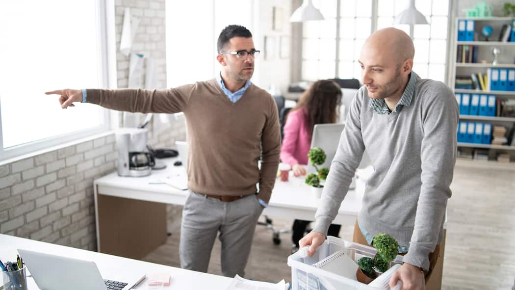Was gilt bei Freistellung? Ein Chef bedeutet seinem Mitarbeiter, das Büro zu verlassen.