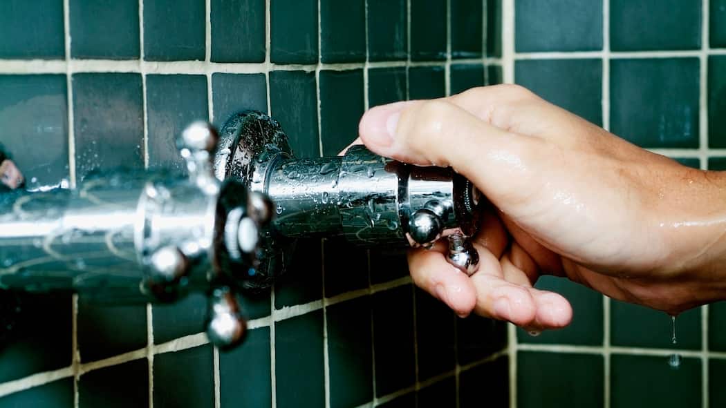 Die Gefahr lauert im Badezimmer Hand dreht in der Dusche den Hahn auf. Unvorsichtiges Energiesparen kann zu Legionellen im Duschwasser führen.