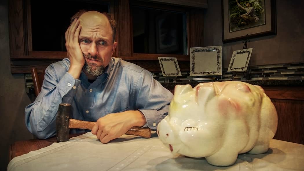 Wovon soll ich Steuern zahlen? Mann schaut mit dem Hammer in der Hand verzweifelt sein Sparschwein an