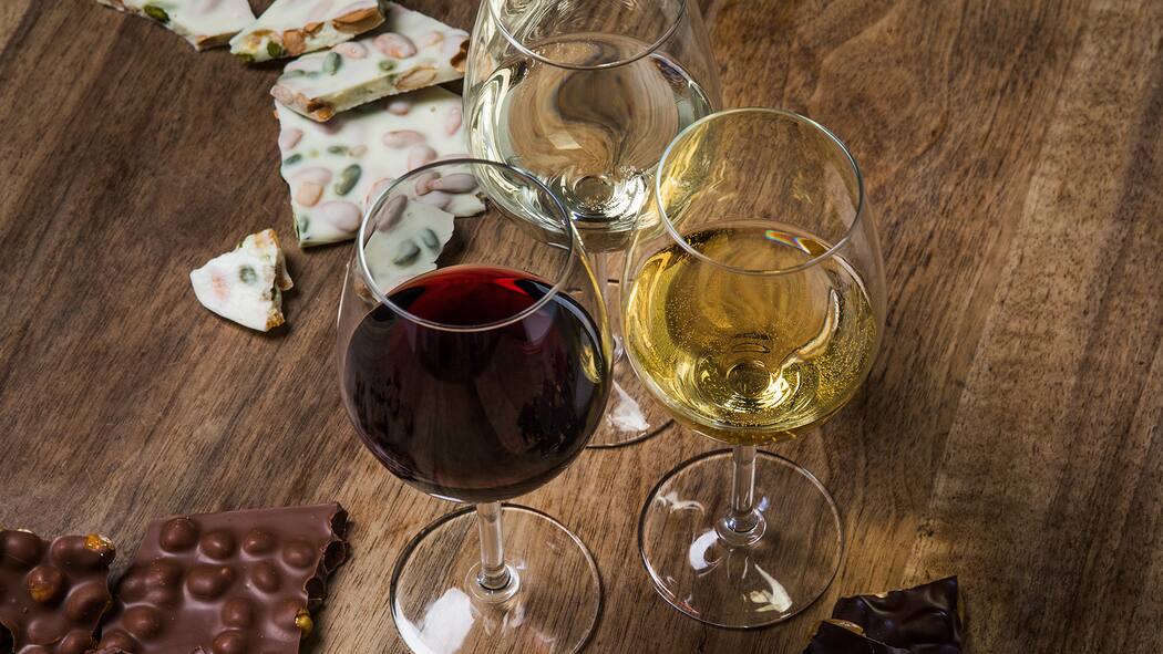 Eine harmonische Kombination Drei Weingläser stehen auf einem Tisch. Daneben liegen verschiedene Schokoladensorten.