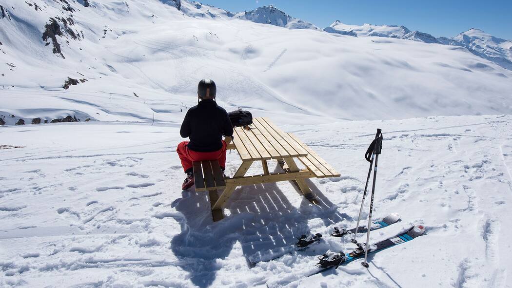 Was gilt bei der Skimiete? Skifahrer sitzt auf einem Bank an einem Tisch neben der Skipiste.