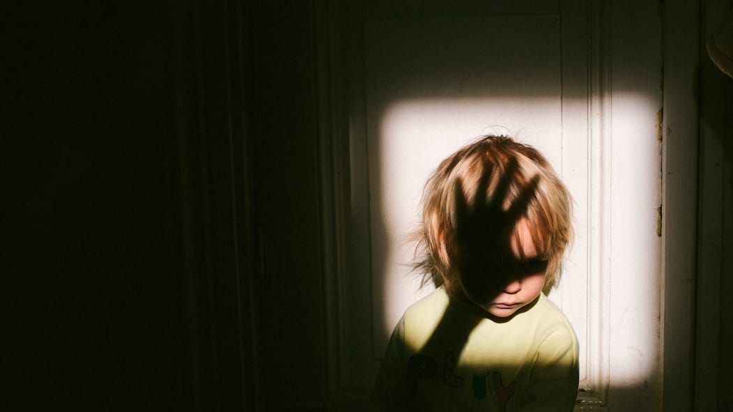 So rutscht die Hand nicht aus Anonymes kleines Kind, das in einem quadratischen Lichtfleck neben einer Tür in einer alten Wohnung sitzt, mit dem Schatten einer Erwachsenenhand über seinem Gesicht.