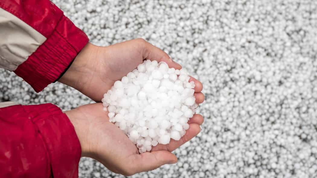 Wann die Versicherung für Hagelschäden zahlt Eine Person hat Hagelkörner in der Hand - Unwetter mit Hagel führen oft zu Schäden an Autos, Gebäuden und Möbeln. Welche Versicherung springt ein, wenn etwas beschädigt wurde