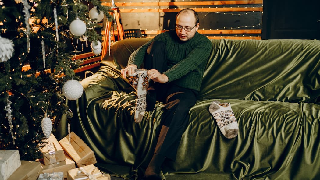 Wohin mit den No-Go-Geschenken? Mann zieht handgestrickte Socken an - Der handgestrickte Kratzpulli, das Duftset, das nach WC-Deo riecht, die Tasse vom falschen FC – nicht alle Geschenke kommen gut an. Mit dem Beobachter werden Sie sie wieder los