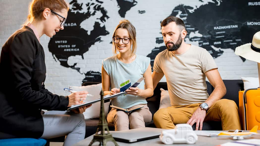 Darf das Reisebüro Gebühren verrechnen? Eine Angestellte eines Reisebüros berät ein junges reisewilliges Paar.