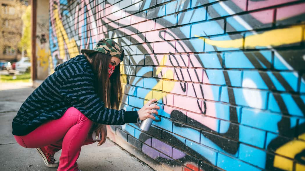 Mit diesen Strafen müssen Jugendliche rechnen Junge Frau mit Bandana sprayt ein Graffiti an eine Wand