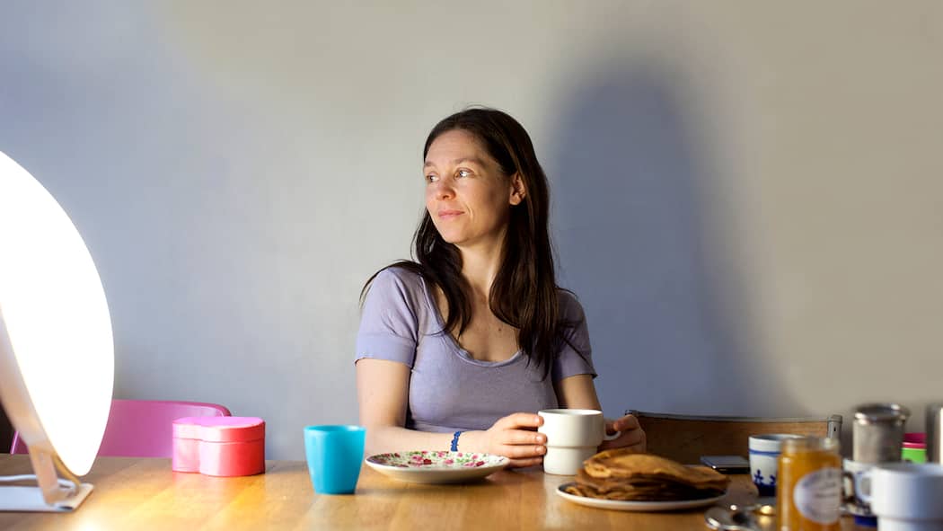 Licht vertreibt den Winterblues Eine Frau sitzt am Frühstückstisch und lässt sich von einer Lichtdusche bescheinen.