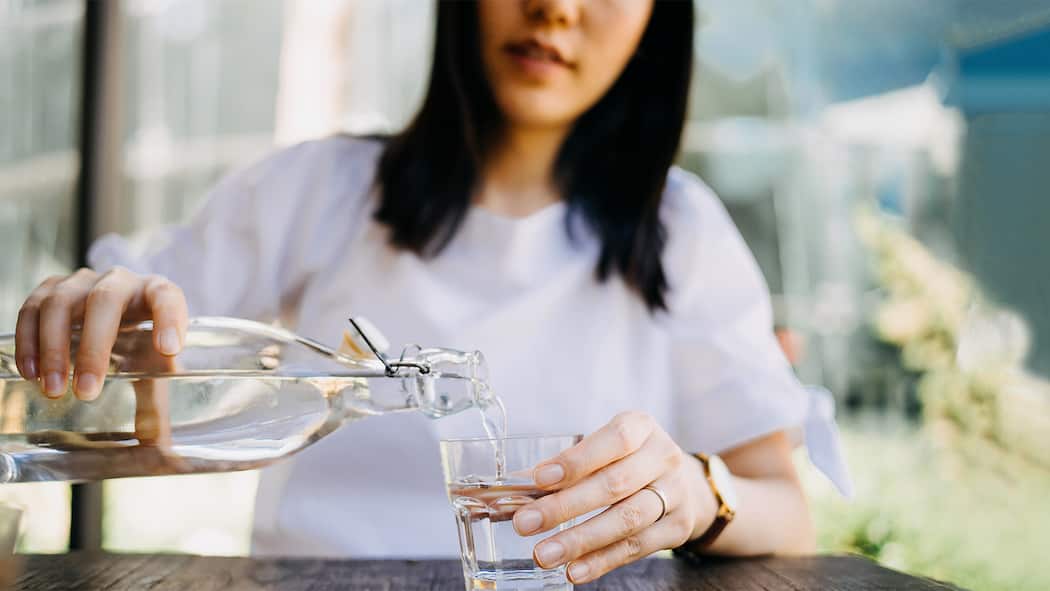 Wasser trinken hilft beim Abnehmen Eine Frau schenkt sich ein Glas Wasser ein.