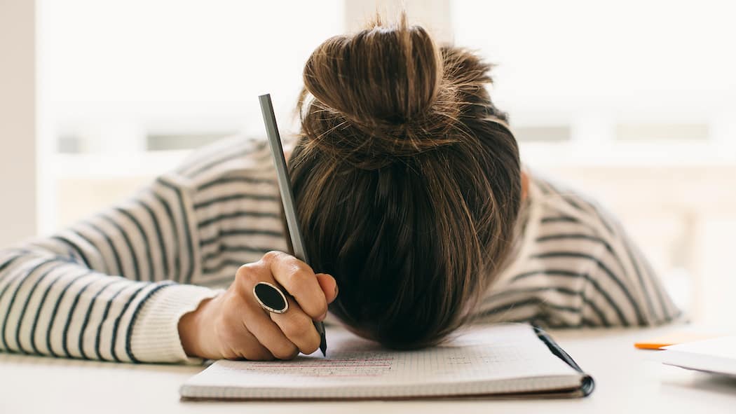 Der Traum vom erholsamen Schlaf Eine Frau legt den Kopf auf ihren Notizblock, während sie den Stift noch in der Hand hält.