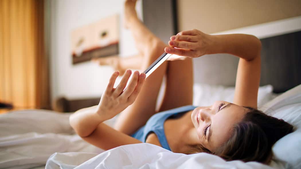 Knipsen, schicken, bereuen – wann sind Nacktbilder strafbar? Jugendliche liegt mit dem Smartphone auf dem Bett