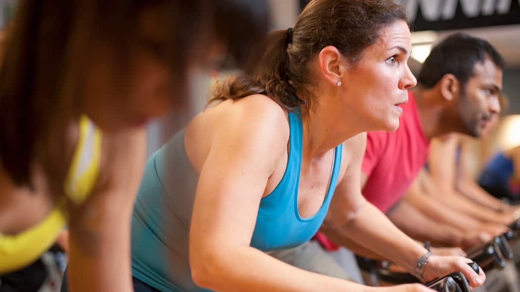 Erste Schritte für Sportmuffel Eine Frau trainiert im Fitnesscenter mit einer Gruppe auf dem Fahrrad.