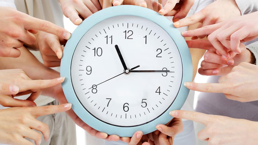 Frist verpasst – was jetzt? In der Mitte liegt eine Uhr, die viertel nach elf anzeigt. Zudem zeigen rund um die Ihr herum viele Hände mit dem Finger auf die Uhr. Beim Ausfüllen der Steuererklärung gelten bestimmte Fristen. Was passiert, wenn man diese nicht einhält?