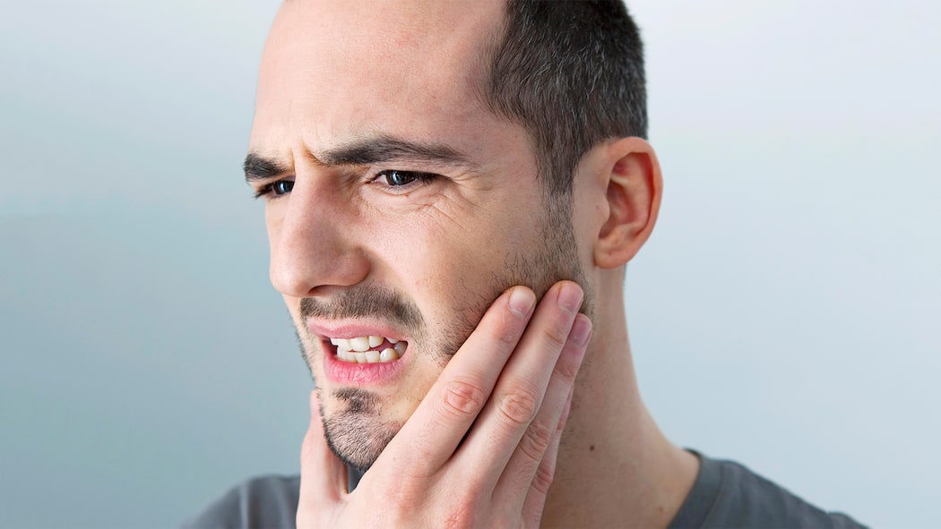 Wer Stress hat, knirscht Ein Mann hält sich den schmerzenden Kiefer, der durch Zähneknirschen entstehen kann.