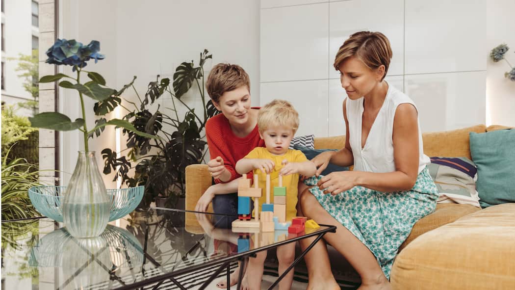 Wenn Kinder die langjährige Freundschaft belasten Zwei Frauen sitzen auf dem Sofa, zwischen ihnen ein kleines Kind am Spielen