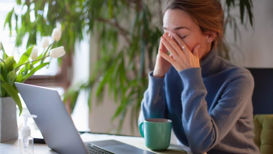 Darf ich im Homeoffice einen zweiten Job annehmen? Eine Frau sitzt zu Hause am Laptop und reibt sich die Augen