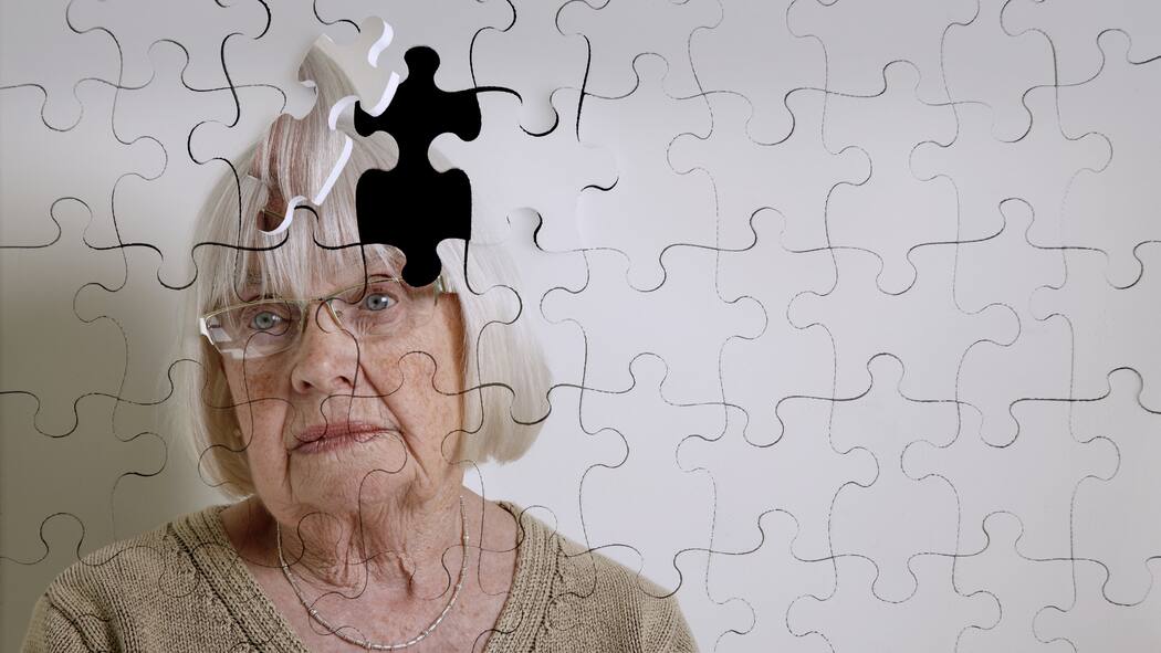 Nur vergesslich – oder schon dement? Eine ältere Frau vor einem Hintergrund, der aussieht wie ein Puzzle, bei dem ein Stück fehlt.