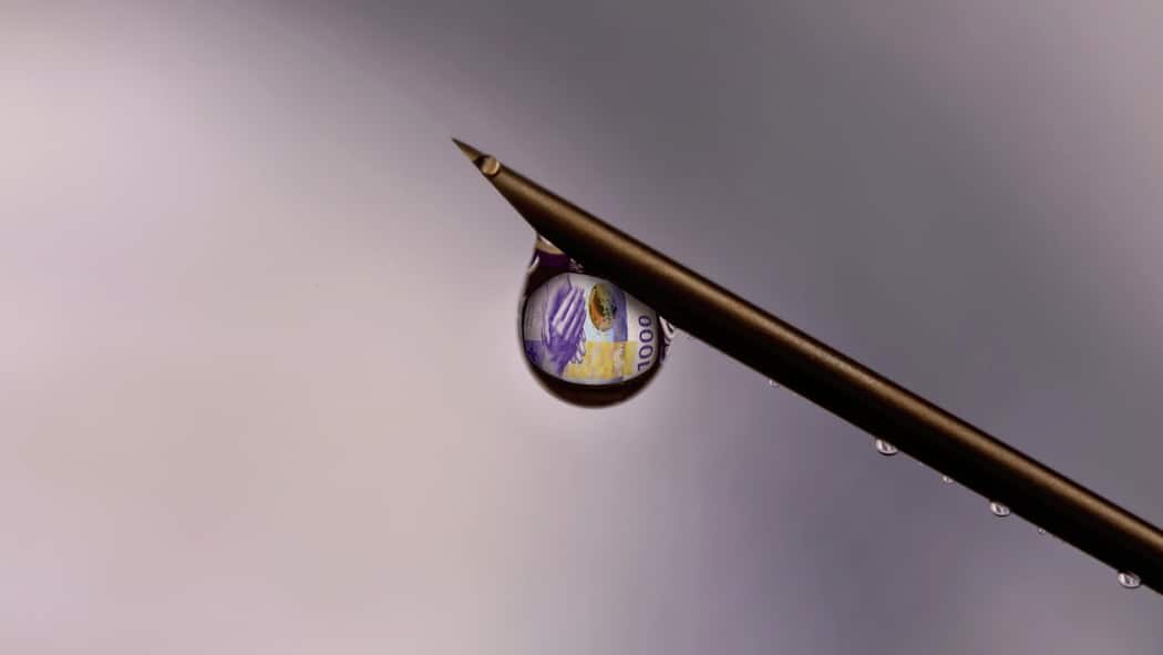 Das Feilschen um Geheimnisse Eine Spritze, aus der ein Tropfen läuft. Darin spiegelt sich eine 1000-Franken-Note.