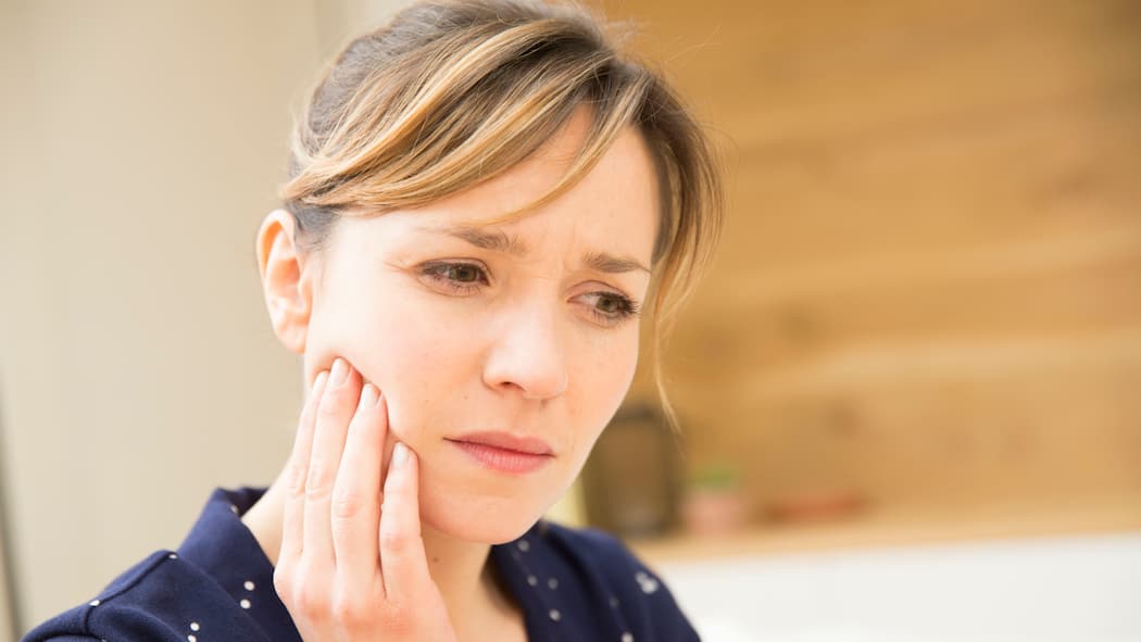 Zahn abgebrochen – zahlt die Versicherung? Eine Frau mit Zahnschmerzen hält sich die Wange