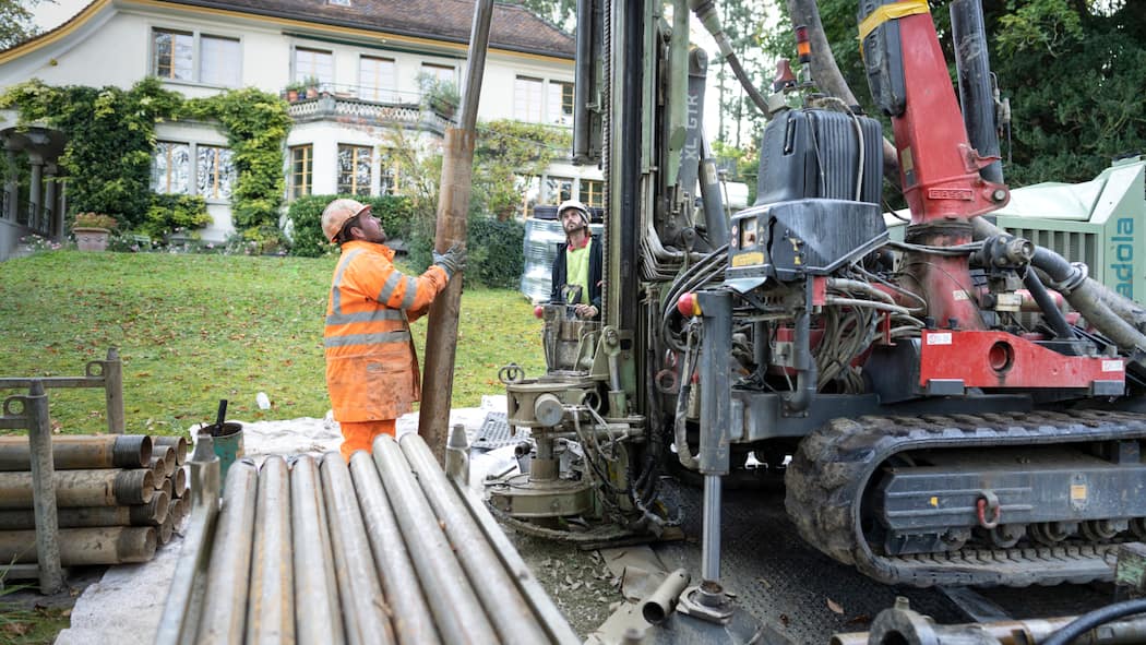 Wie der Wechsel beim Eigenheim gelingt Zwei Mitarbeiter eines Bauunternehmens bohren für eine Wärmepumpe mit Erdsonde in einem Garten eines Hauses.
