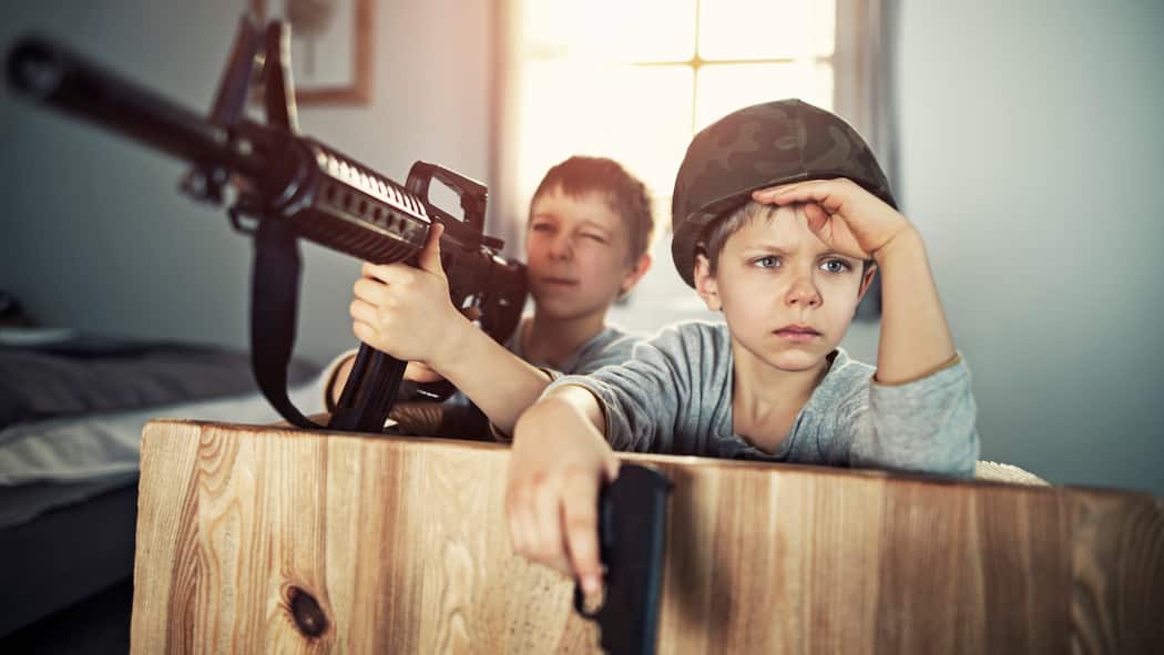 Kind will Krieg spielen – wie sollen Eltern reagieren? Zwei junge Buben spielen Soldaten in der Stube mit Spielzeugwaffen