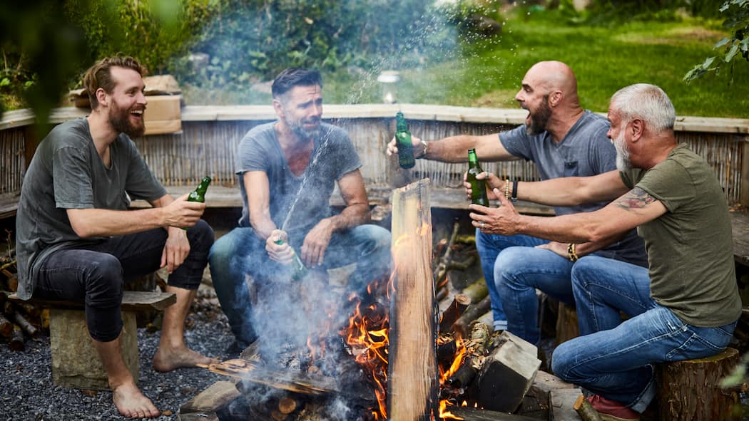 Wie reagieren bei frauenfeindlichen Sprüchen? Vier Männer sitzen draussen an einem Feuer, trinken Bier und lachen