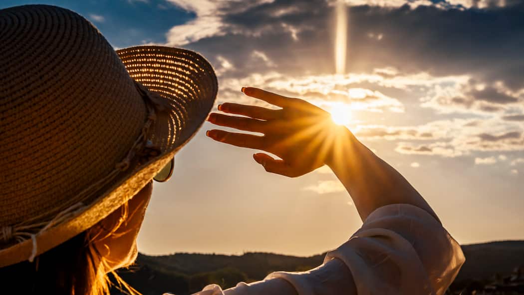 Hautfeind Sonne Eine Frau mit Sonnenhut und Sonnenbrille hält sich schützend die Hand vors Gesicht, um nicht von der Sonne geblendet zu werden