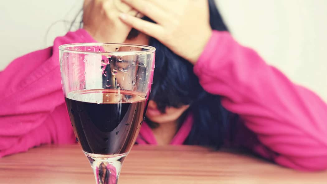 Wenn Rotwein für rote Köpfe sorgt Eine Frau sitzt vor einem Glas Rotwein und hält sich den Kopf