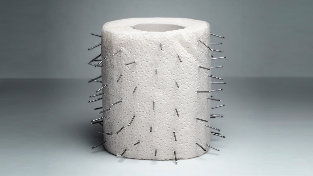 Was tun bei analen Beschwerden? In einer Rolle Toilettenpapier stecken kleine Nägel, welche symbolisieren, wie schmerzhaft Hämorrhoiden sein können.