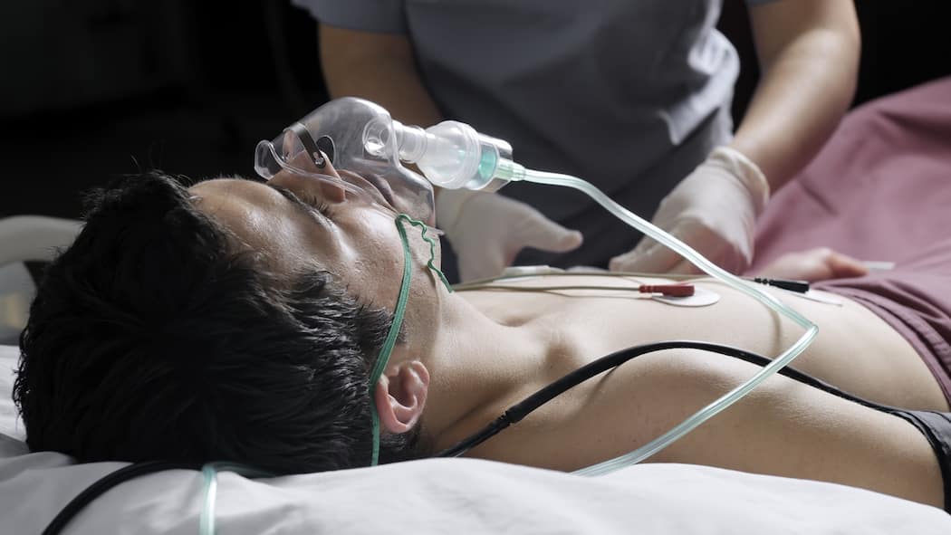 Checkliste für Ihre Patientenverfügung Ein Mann mit einer Sauerstoffmaske liegt in einem Bett und wird von einer Person mit Handschuhen betreut.