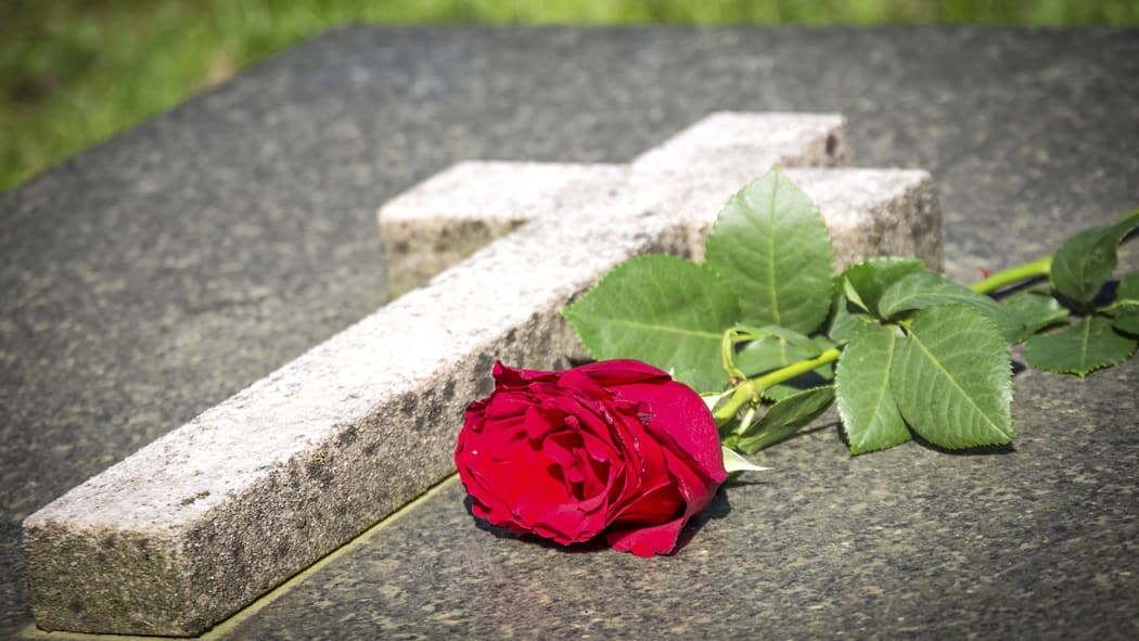 Was nach einem Todesfall getan werden muss steinernes Grab mit einem Kreuz, auf dem eine rote Rose liegt
