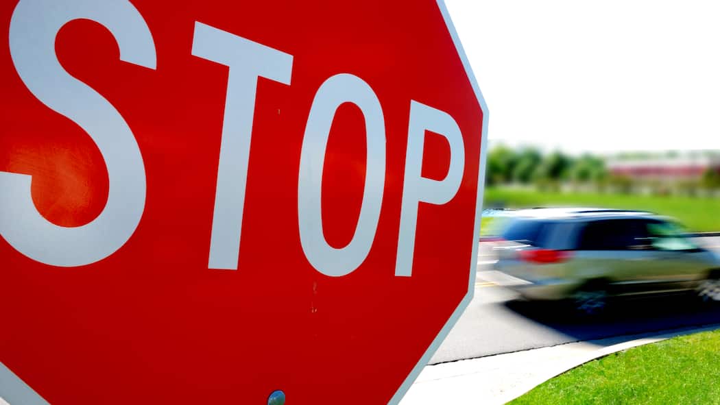 Welche Busse droht? Stop-Schild im Vordergrund, vorbeifahrendes Auto im Hintergrund