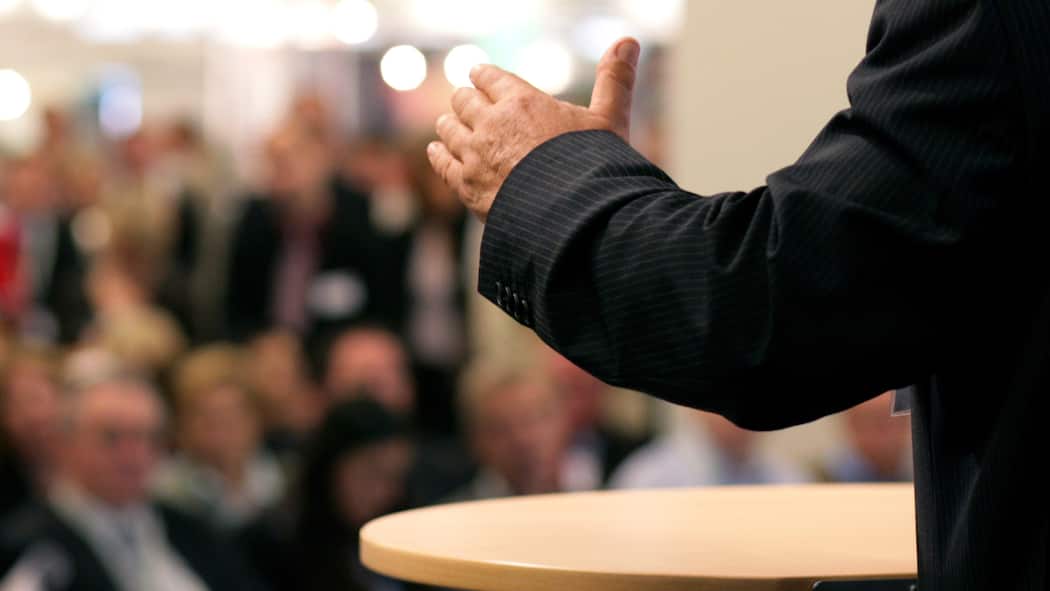 So wird die Generalversammlung ein Erfolg Mann in Anzug vor Versammlung Fokus auf linkem Arm, der leicht angehoben ist