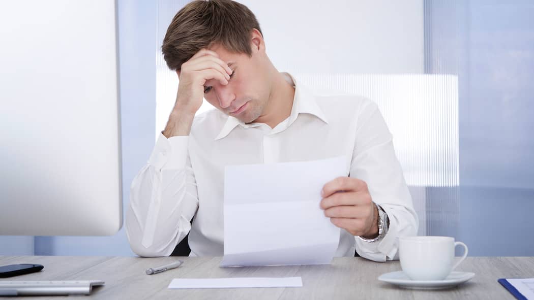 Muss ich fürs Inkasso zahlen? Geschäftsmann sitzt am Schreibtisch und studiert Unterlagen.