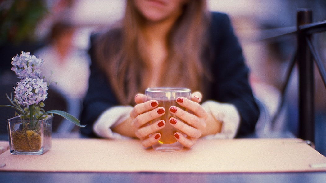 Besser Tee trinken statt abwarten Eine junge Frau hält ein Glas Tee in der Hand.